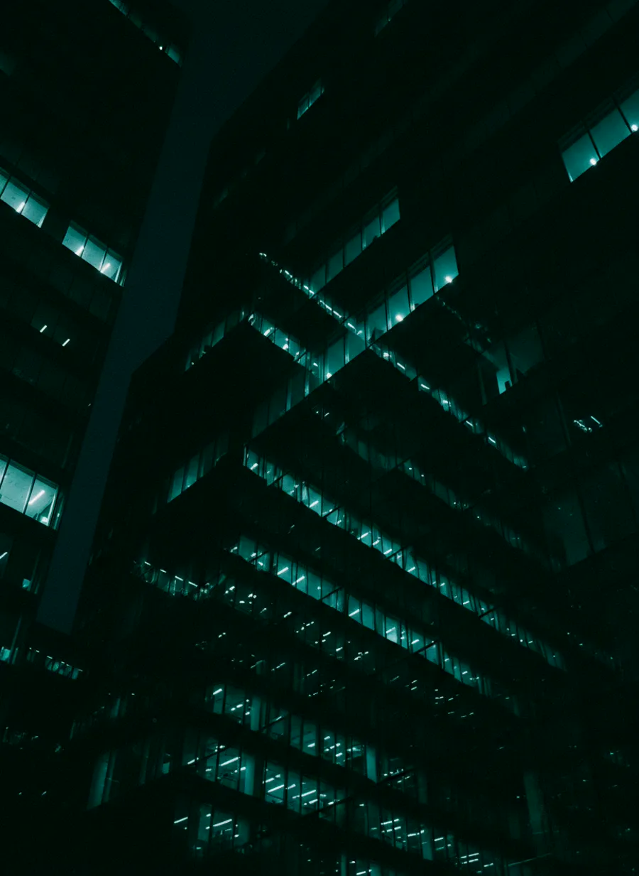 A glass office tower at night, most of its floors dark and a few still lit